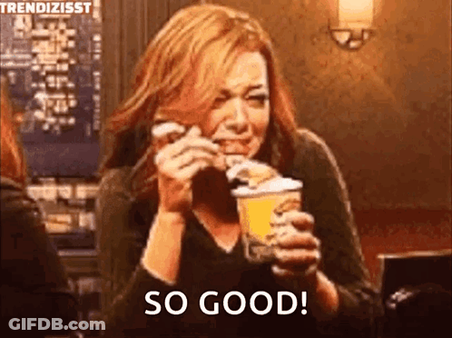 A Woman Is Eating A Hamburger And Holding A Cup Of Ice Cream And Saying So Good . GIF