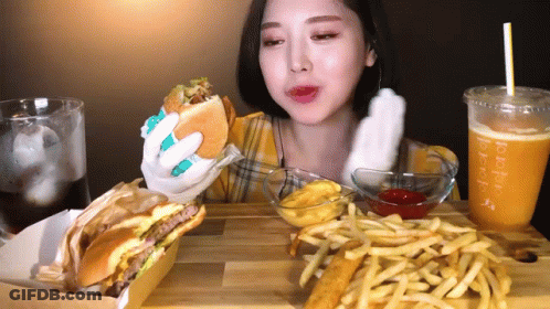 A Woman Is Eating A Hamburger , French Fries And A Drink . GIF