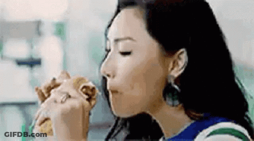 A Woman Is Eating A Hamburger In A Restaurant . GIF