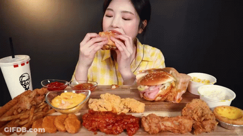 A Woman Is Eating A Hamburger On A Cutting Board With A Kfc Drink GIF