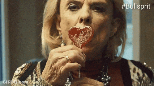 A Woman Is Eating A Heart Shaped Lollipop With The Hashtag Bullsprit GIF