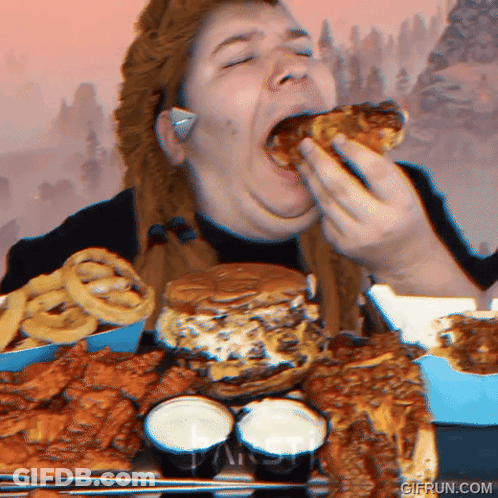 A Woman Is Eating A Large Amount Of Food Including A Hamburger Onion Rings And Wings GIF