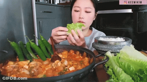 A Woman Is Eating A Leaf Of Lettuce From A Pot Of Food GIF