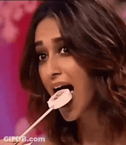 A Woman Is Eating A Lollipop With A Smiley Face On It GIF