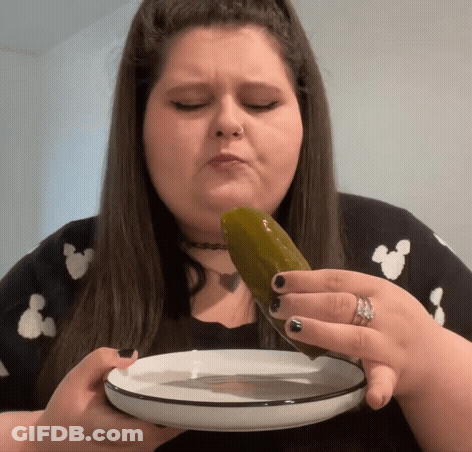 A Woman Is Eating A Pickle From A Plate With A Knife . GIF
