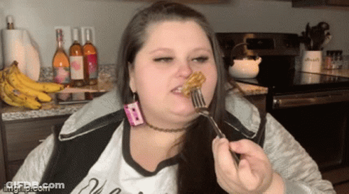 A Woman Is Eating A Piece Of Food With A Fork In Front Of Bottles Of Wine And Bananas GIF
