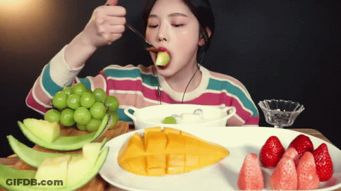 A Woman Is Eating A Piece Of Fruit With A Spoon In Her Mouth GIF