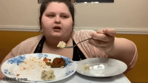 A Woman Is Eating A Plate Of Food With A Fork And Spoon GIF