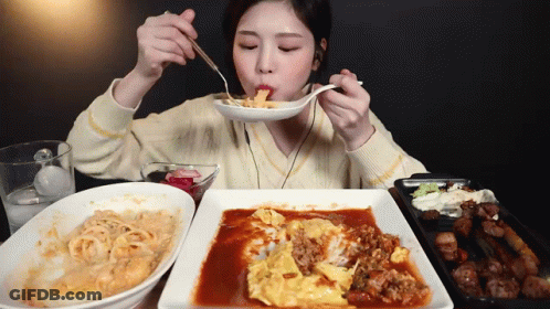 A Woman Is Eating A Plate Of Food With A Spoon And Fork GIF