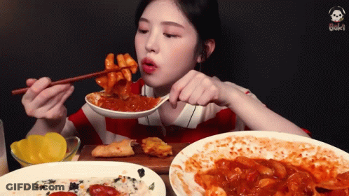 A Woman Is Eating A Plate Of Food With Chopsticks GIF
