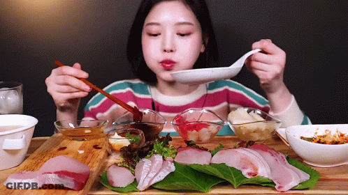 A Woman Is Eating A Plate Of Food With Chopsticks And A Spoon GIF