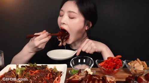 A Woman Is Eating A Plate Of Food With Chopsticks And A Spoon GIF
