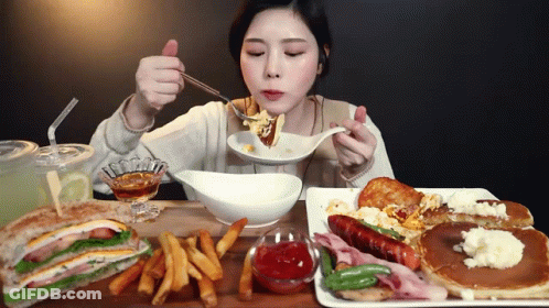 A Woman Is Eating A Sandwich And Pancakes At A Table GIF