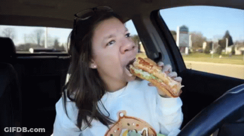 A Woman Is Eating A Sandwich In A Car . GIF