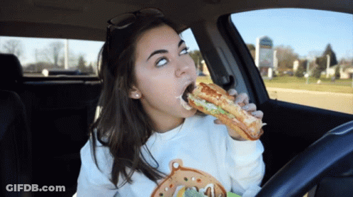 A Woman Is Eating A Sandwich While Driving GIF
