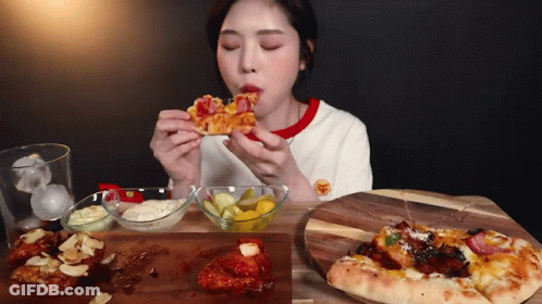 A Woman Is Eating A Slice Of Pizza Next To A Plate Of Pickles GIF