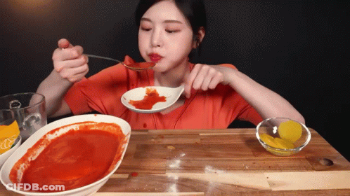 A Woman Is Eating A Spoonful Of Sauce From A Bowl GIF