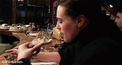 A Woman Is Eating An Oyster While Sitting At A Table In A Restaurant GIF