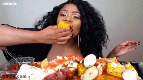 A Woman Is Eating Corn On The Cob With A Youtube Eat With Que Logo Behind Her GIF