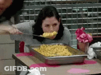 A Woman Is Eating Food From A Tray With A Spoon GIF
