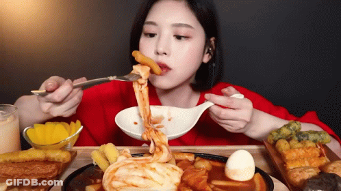 A Woman Is Eating Food With A Fork And Spoon . GIF