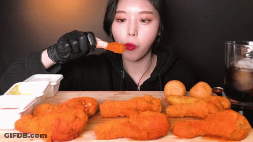 A Woman Is Eating Fried Chicken While Wearing Gloves GIF