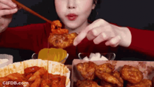 A Woman Is Eating Fried Chicken With Chopsticks And A Spoon . GIF