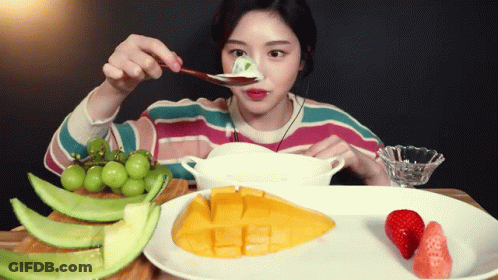 A Woman Is Eating Fruit With A Spoon And A Bowl GIF