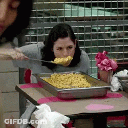 A Woman Is Eating Macaroni And Cheese With A Spoon In Her Mouth GIF
