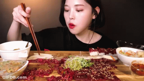 A Woman Is Eating Meat With Chopsticks While Wearing Ear Buds GIF