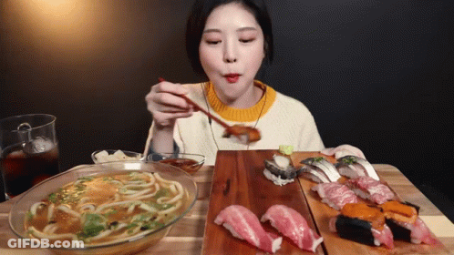 A Woman Is Eating Noodles And Sushi With Chopsticks At A Table GIF