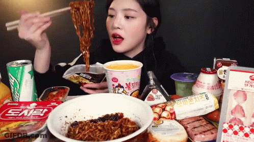 A Woman Is Eating Noodles With Chopsticks While Sitting At A Table Filled With Food . GIF