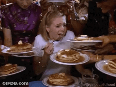 A Woman Is Eating Pancakes With A Fork While A Group Of People Are Holding Plates Of Pancakes . GIF