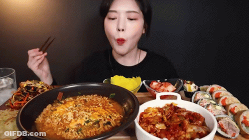 A Woman Is Eating Ramen And Sushi With Chopsticks . GIF