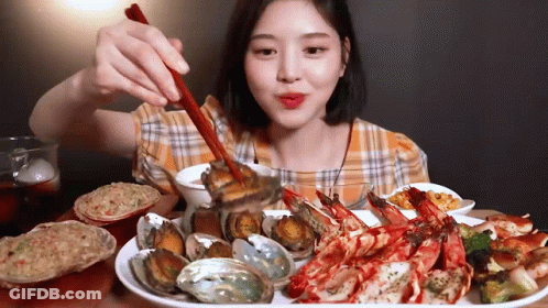 A Woman Is Eating Seafood With Chopsticks And A Spoon . GIF