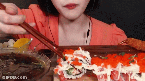A Woman Is Eating Sushi With Chopsticks While Wearing Ear Buds GIF