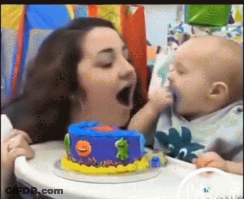 A Woman Is Feeding A Baby A Birthday Cake With A Frog On It . GIF