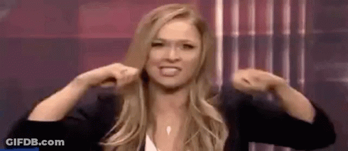 A Woman Is Flexing Her Muscles In Front Of A Curtain . GIF