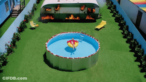 A Woman Is Floating In A Swimming Pool In Front Of A Trailer That Is On Fire GIF