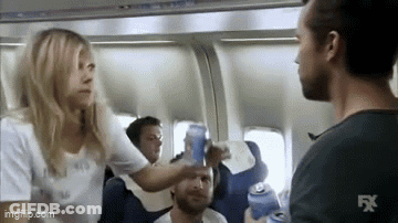 A Woman Is Giving A Man A Beer On An Airplane . GIF