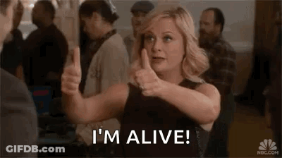 A Woman Is Giving A Thumbs Up And Saying `` I 'M Alive '' In A Crowded Room . GIF