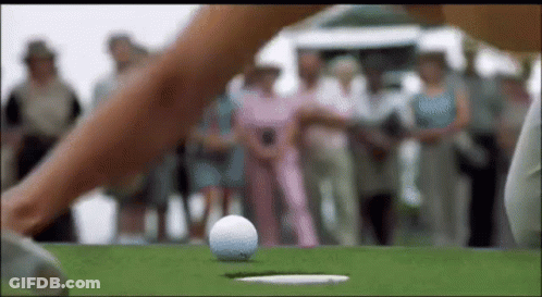 A Woman Is Hitting A Golf Ball Into A Hole . GIF
