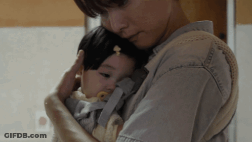 A Woman Is Holding A Baby In A Carrier GIF