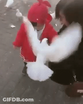A Woman Is Holding A Baby In Her Arms And A Pigeon Is Flying Away From Her . GIF