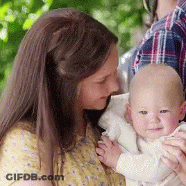 A Woman Is Holding A Baby In Her Arms And The Baby Is Smiling For The Camera . GIF