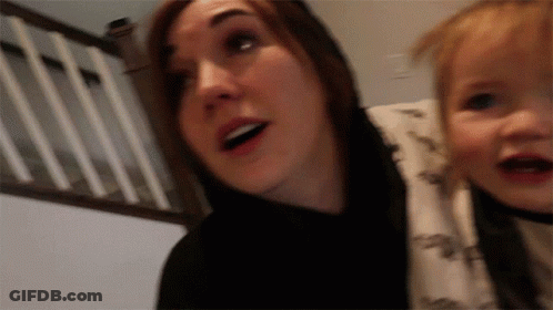 A Woman Is Holding A Baby In Her Arms And The Baby Is Wearing A Dinosaur Shirt GIF