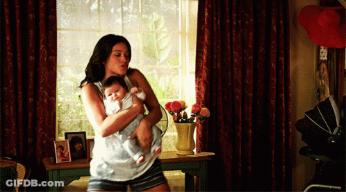 A Woman Is Holding A Baby In Her Arms In A Room GIF