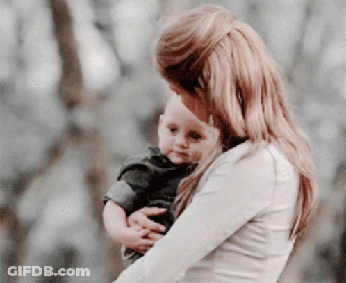 A Woman Is Holding A Baby In Her Arms Outdoors GIF