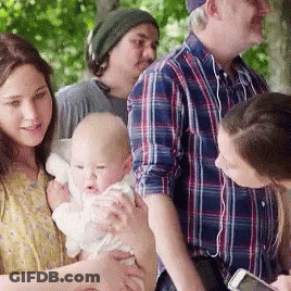 A Woman Is Holding A Baby In Her Arms While A Man Looks At His Phone GIF