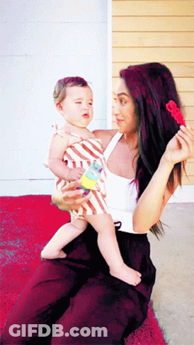 A Woman Is Holding A Baby In Her Lap And Holding A Toy In Her Hand GIF